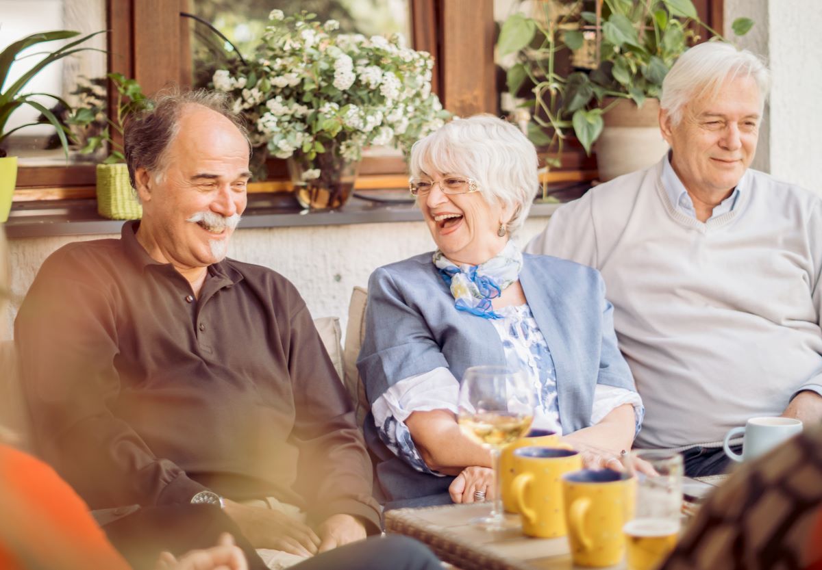 Three friends seated outside a resaurant laughing and smiling